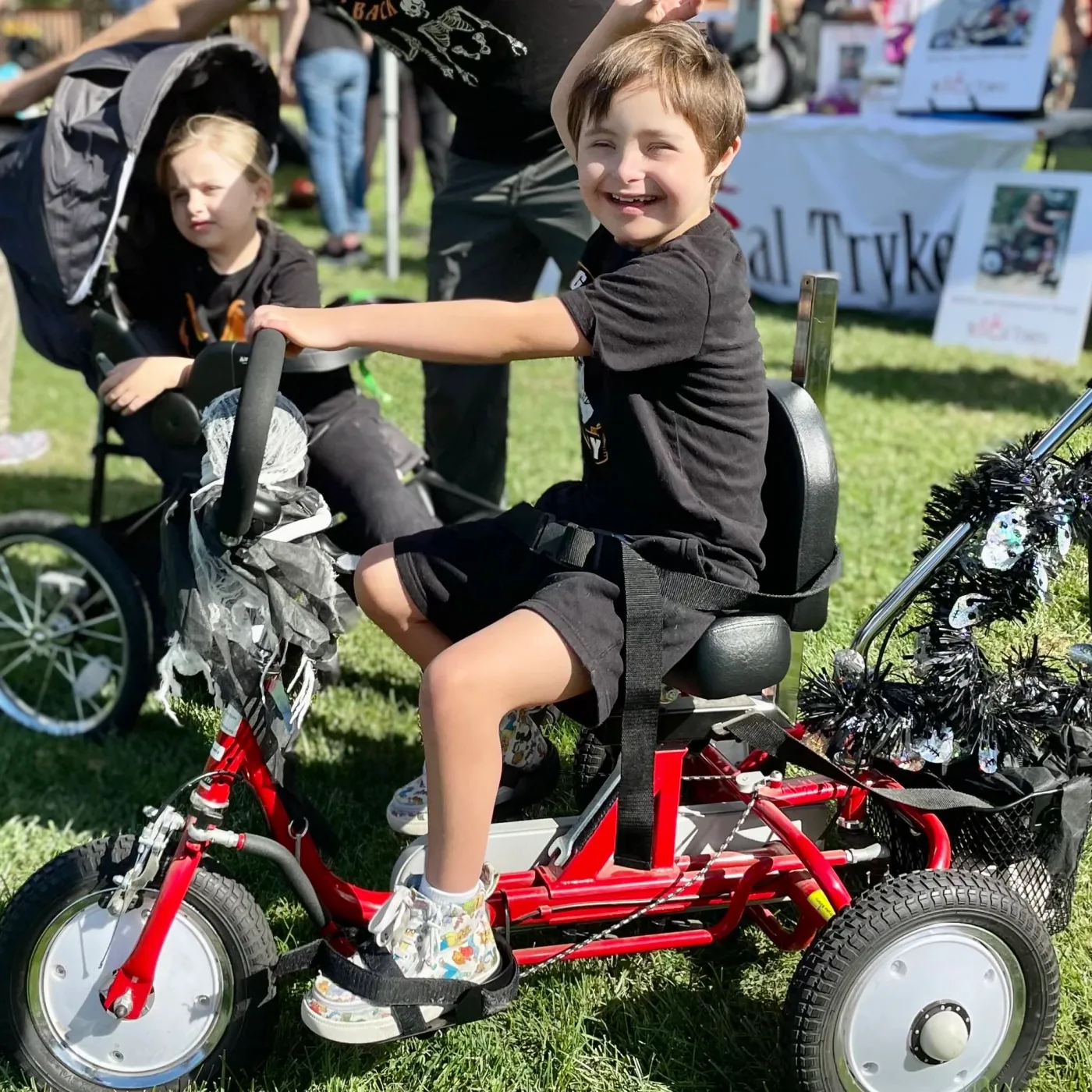 A child seated on a red adaptive tricycle at the festival, with another rider nearby.